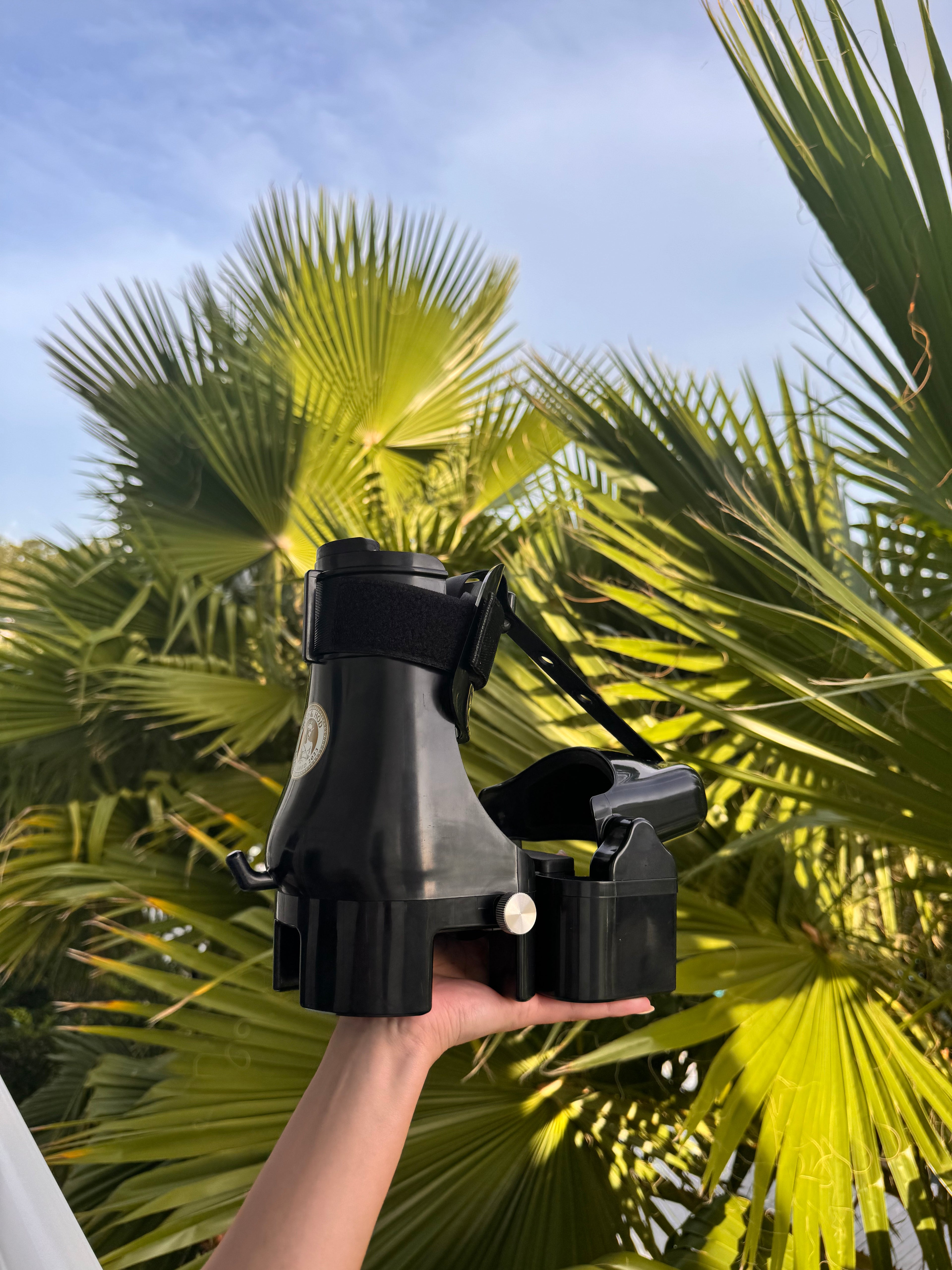 Person holding a black device against a backdrop of palm trees